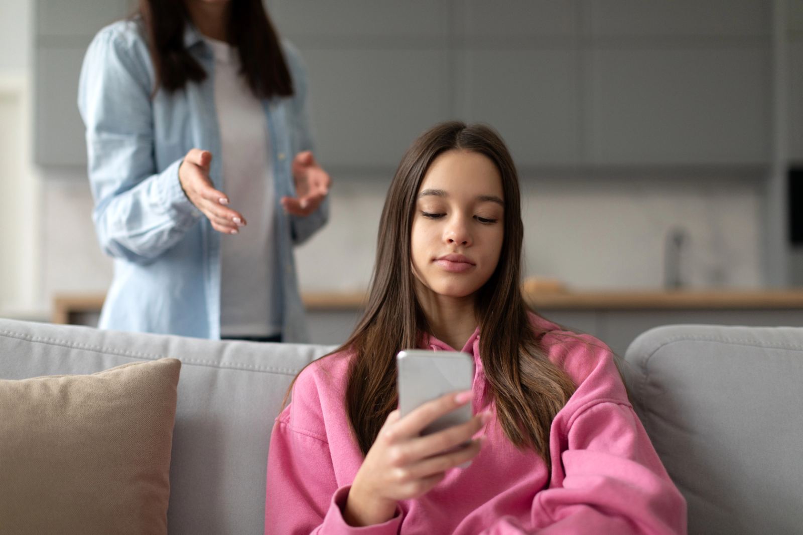 Mutter spricht ruhig mit Teenager-Tochter, die aufs Handy schaut